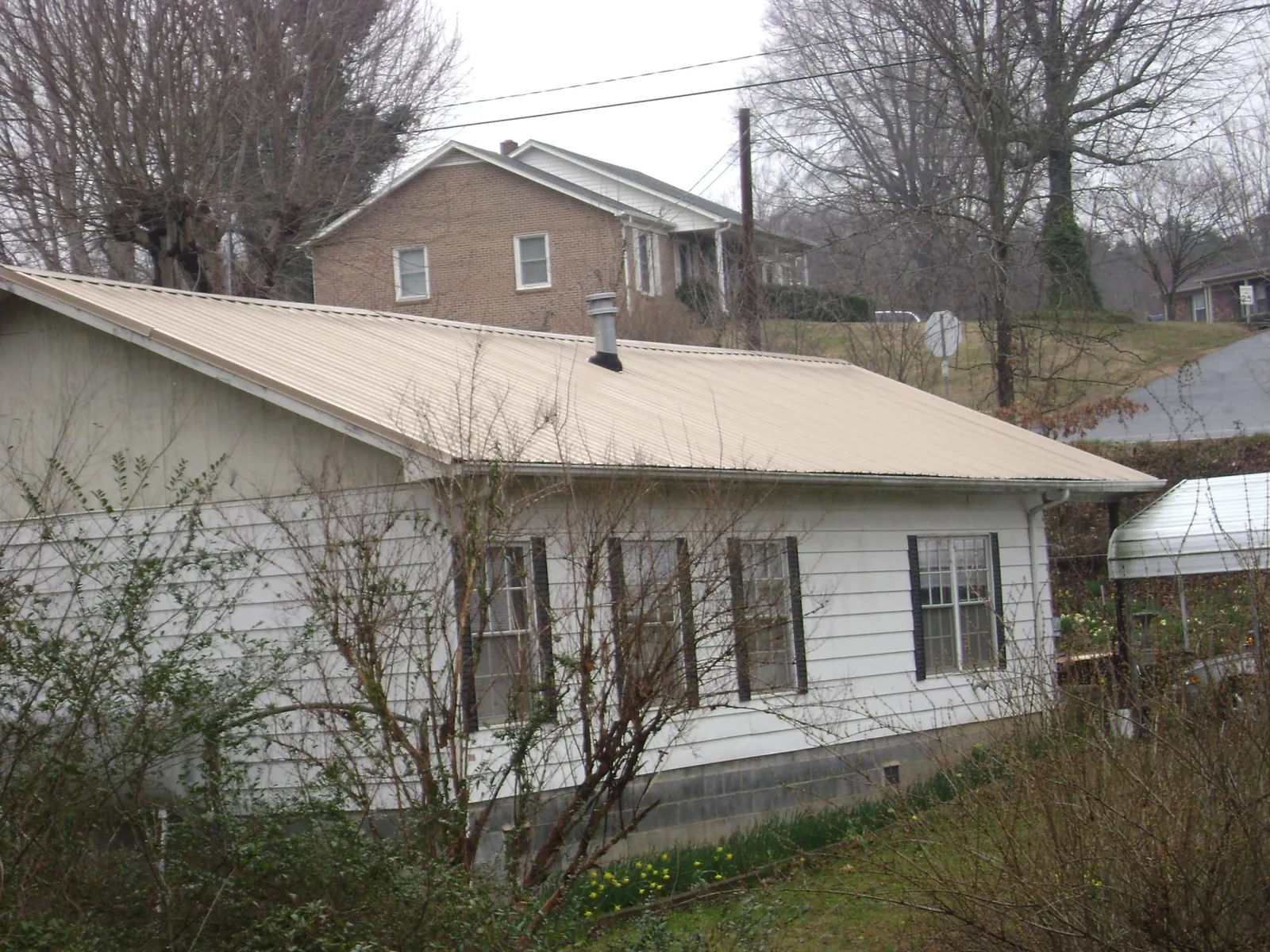 Tan metal roof on a white sided house set into a hillside — Commercial Roofing by Roofing Brothers in Wallace